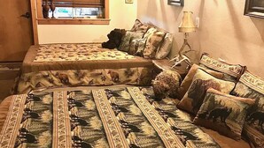 A bedroom with two beds, each with a patterned bedspread featuring animal prints. There is a window with blinds, a lamp on a bedside table, and a wall-mounted light fixture. - The Ultimate Escape  (Heron)