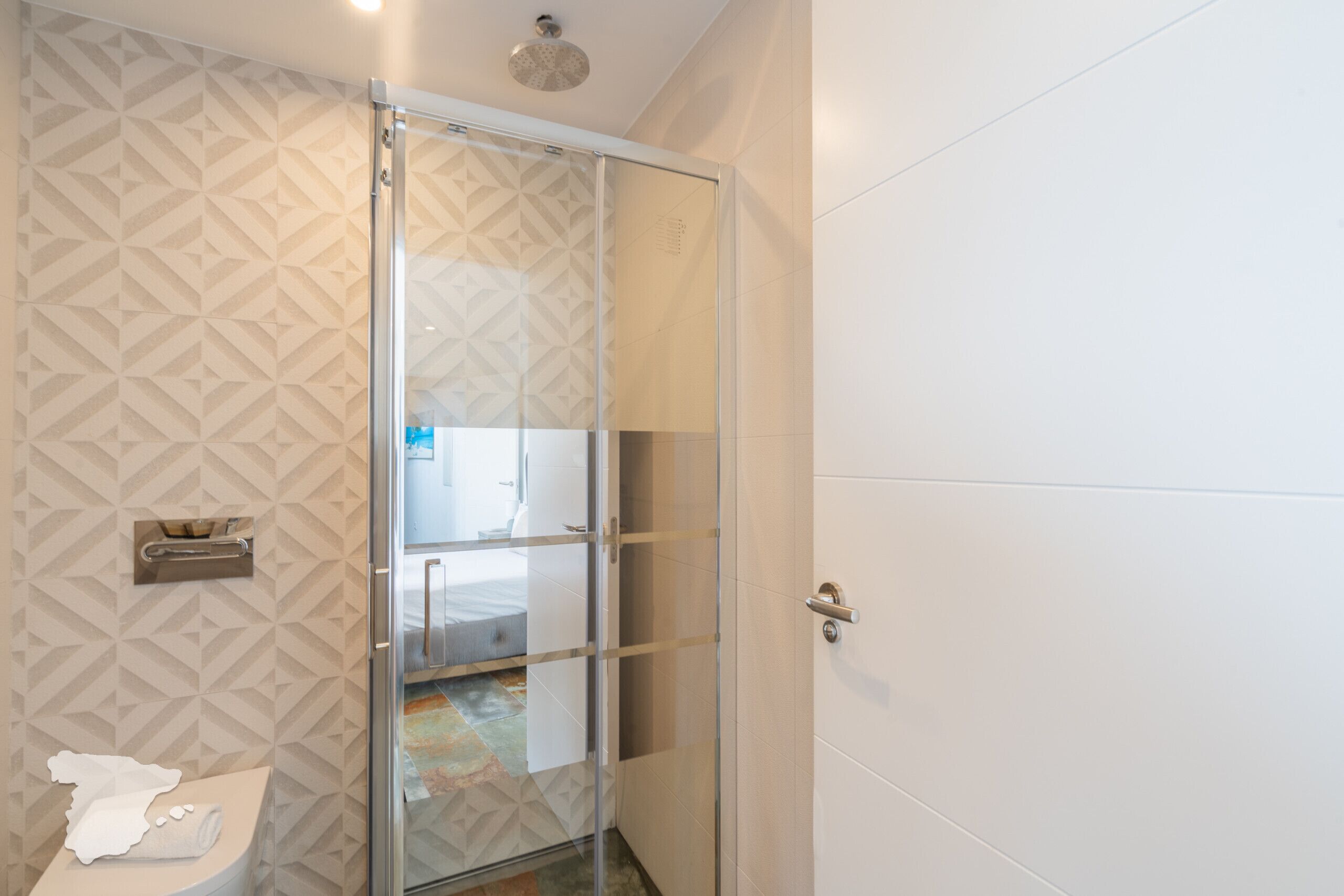 Een badkamer met een douchecabine van glas, een toilet met een handdoek, en een muren met een patroon.