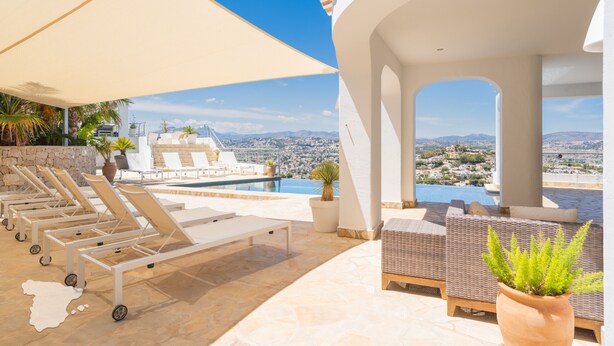 Un área de piscina en la azotea con sillones, una sombrilla grande y vistas a la ciudad y montañas.