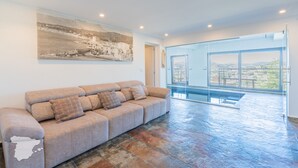 Un espacio habitable amplio con un sofá color beige, un ventanal grande y suelo de piedra.