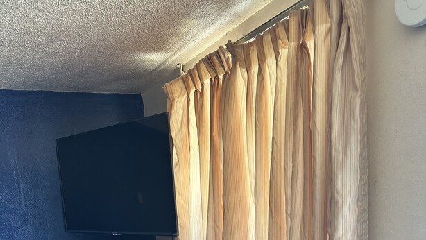 A compact room with a flat-screen TV mounted on a wall, a small white refrigerator, and a wall-mounted air conditioner.