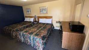 A hotel room with two beds, a desk, a chair, a heater, and two framed pictures on the wall.