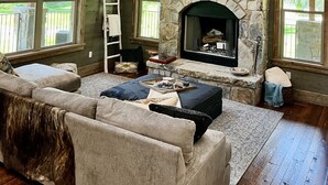 Una sala de estar con chimenea de piedra, un televisor grande montado encima y un candelabro.