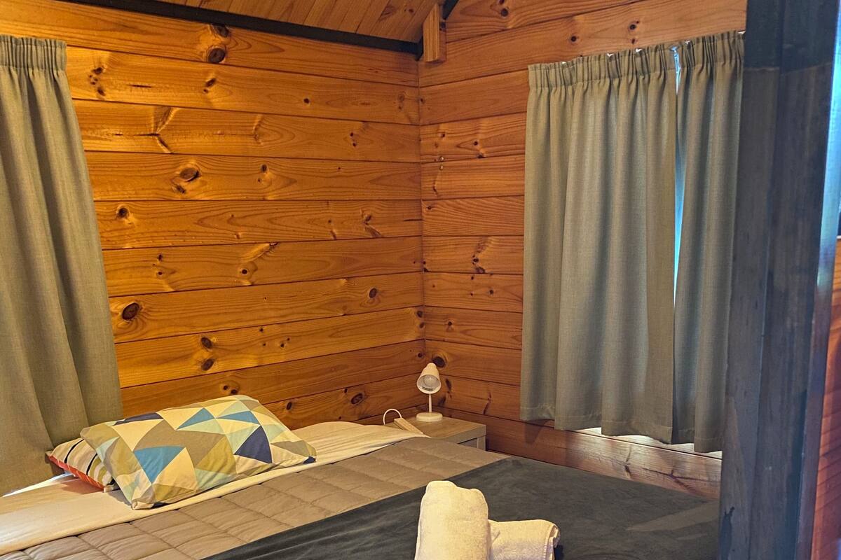 A wooden cabin room with a bed, a bedside lamp, and curtains.