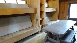L'intérieur d'une cabane en bois, avec un lit superposé, une table et des étagères.