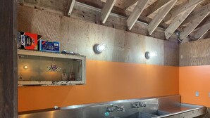 Des toilettes publiques avec un plafond en bois, des murs orange et un lavabo en acier inoxydable.