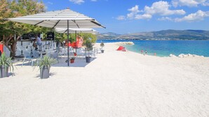 Un café situé en bord de mer, avec une terrasse, une tente rouge et une vue sur la mer et les montagnes.