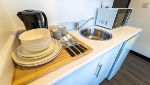 Una kitchenette con un lavabo, microondas, cafetera y platos apilados.