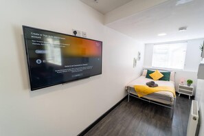 A modern hotel room with a bed, a bedside table, a small desk, and a wall-mounted TV displaying a sign-in screen. - Large Studio available on First floor! (Birmingham)