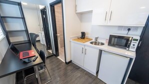 Eine kleine Küche mit Mikrowelle, Spüle und einer Arbeitsplatte. Auf einem Schreibtisch mit Stuhl steht ein Laptop.