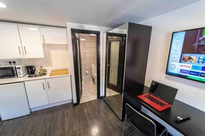 A modern kitchen with white cabinets, a microwave, and a coffee maker. There is a laptop on a desk with a TV displaying Netflix options.