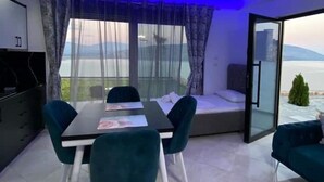 A modern dining area with a table and chairs, a sofa, and a view of the sea. - Welcome to ILLYRIAN PARADISE. Near beach and Lake Views. (Ksamil)