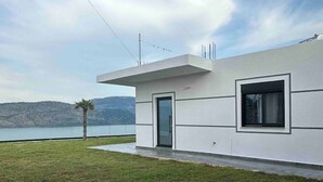 A modern house with a flat roof, a large window, and a door. - Welcome to ILLYRIAN PARADISE. Near beach and Lake Views. (Ksamil)
