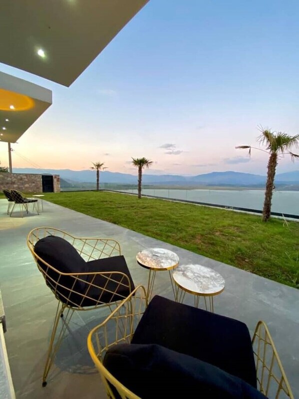 An outdoor seating area with chairs and tables, overlooking a body of water and mountains.