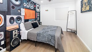 Une chambre à coucher comprenant un lit, un ventilateur de plafond, un radiateur et un mur décoré avec un motif représentant un haut-parleur.