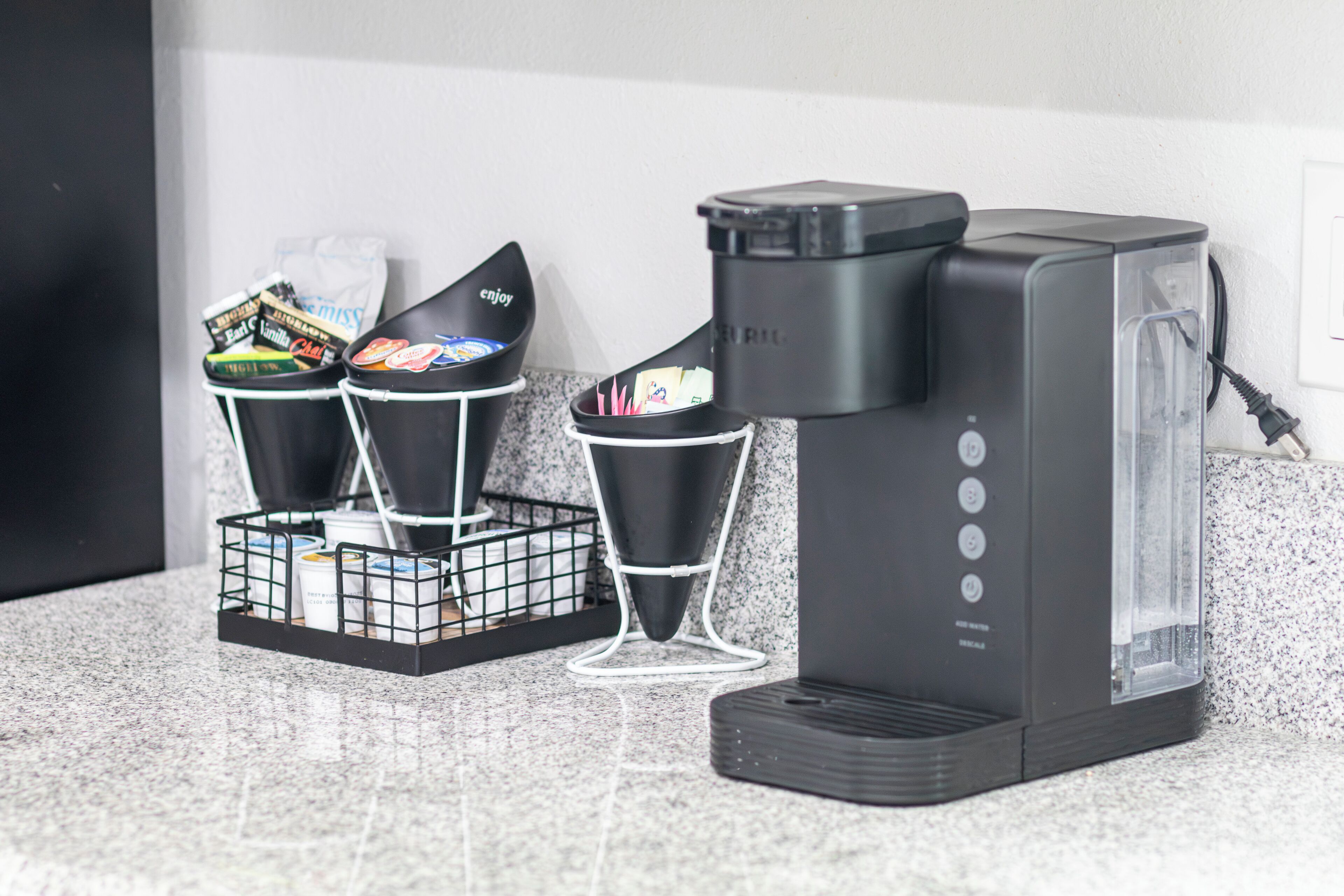Eine Kaffeemaschine mit transparentem Wasserbehälter, einem schwarzen Auffangbehälter und einem Filterkorb mit Einwegbechern.
