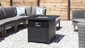 Un espace extérieur aménagé avec une table-grill noire, des canapés gris et des fauteuils en osier.