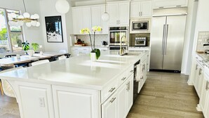 Een moderne keuken met witte kasten, roestvrijstalen apparatuur en een groot kookeiland.