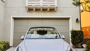 Een witte auto geparkeerd voor een huis met een garage, een balkon en een kleine boom.