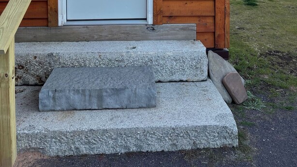 Una cabaña de madera con puerta blanca, número 3, y un pequeño porche con escalones que llevan a la puerta.