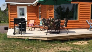 Una casa de madera con un patio, una parrilla y mobiliario exterior.