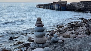 Escena costera con una pila de piedras al frente y un muelle que se adentra en el agua.