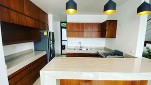 Een moderne keuken met houten kastjes, een marmeren aanrechtblad, een centraal kookeiland en hanglampen.