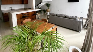 Een moderne keuken met witte kastjes, een eethoek met een houten tafel en een grijze bank.