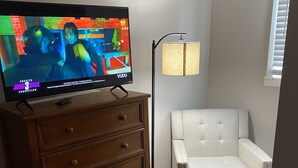 Un televisor sobre un aparador de madera, una lámpara de pie y un sillón blanco en una habitación con suelo de madera.