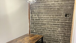 Un comedor con una mesa de madera y bancos, una lámpara colgante y una pared de ladrillo.