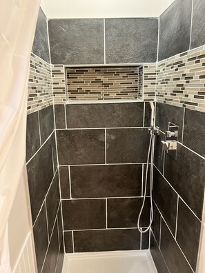 Un espace douche avec des carreaux de couleur foncée et une étagère carrelée au-dessus de la douche.