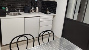 A compact kitchen with a microwave, coffee maker, and sink. There is a small dining area with a table and chairs. - L'escapade Enchantée Paris-disneyland (Noisy-le-Grand)