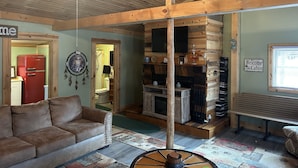 A cabin interior with a wooden ceiling, a red refrigerator, a brown sofa, a wooden bench, and a welcome sign.