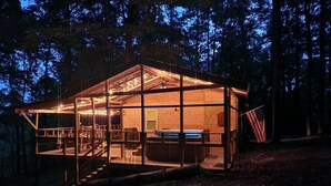 A cabin with a glass enclosure, a hot tub, and an American flag outside.