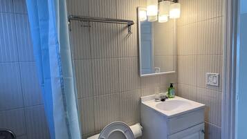 Baño con inodoro, lavamanos, espejo y cortina de ducha.