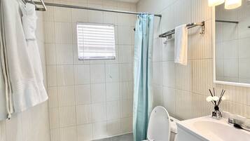Een badkamer met douche, toilet, wastafel en een spiegel met verlichting.