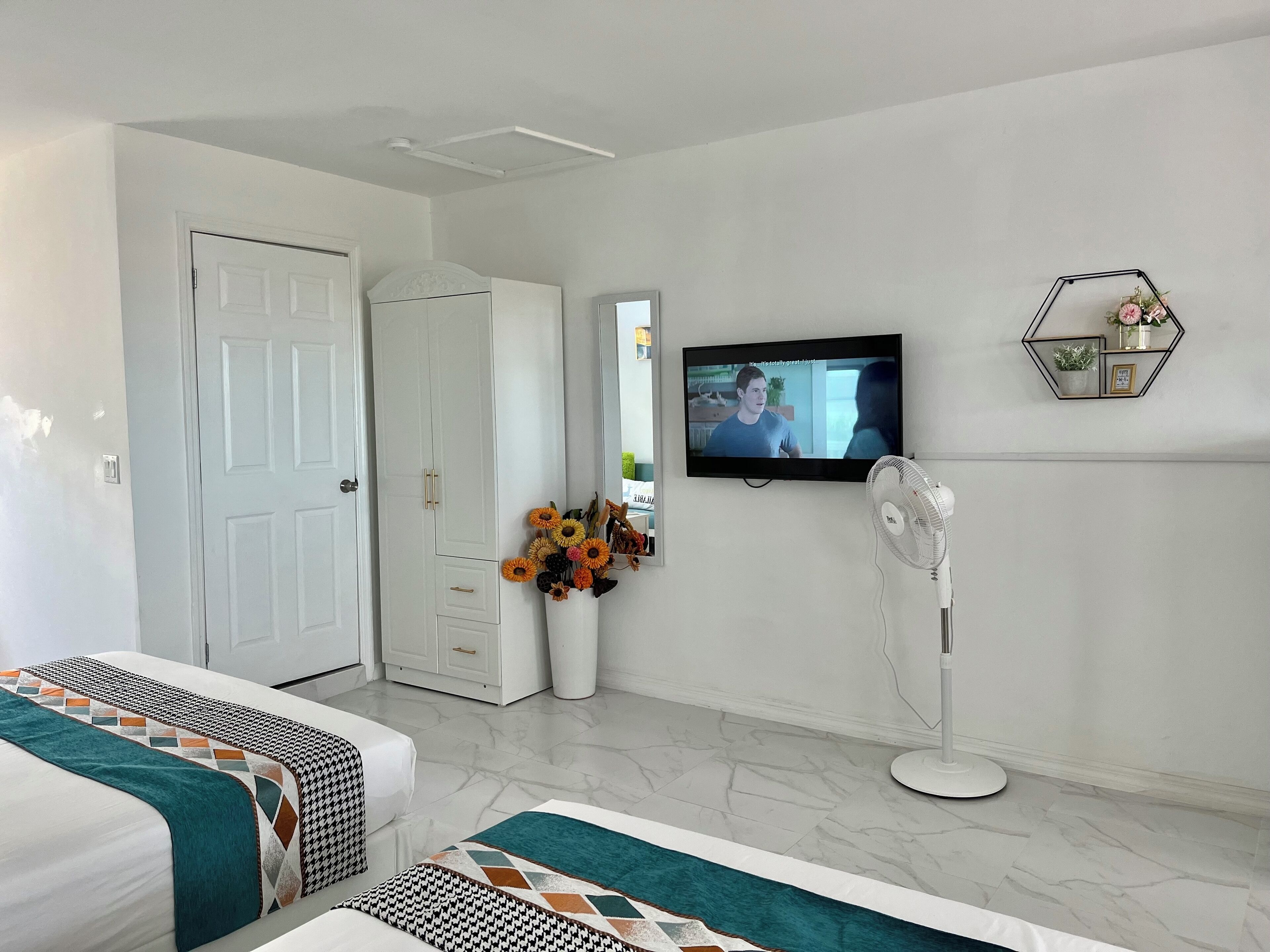 A hotel room with two beds, a TV, a mirror, a white wardrobe, and a decorative shelf.