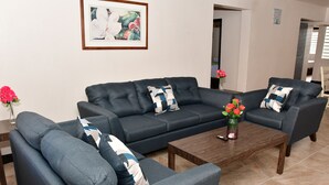 Ein modernes Wohnzimmer mit einer dunkelgrauen Sofagarnitur, einem Holztisch und einem gerahmten Blumenbild an der Wand.