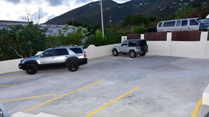 Ein Parkplatz mit zwei Geländewagen und einem Lieferwagen, umgeben von einer weißen Mauer und Grünflächen.