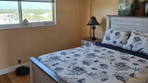A bedroom with a bed, a ceiling fan, a window with a view, a nightstand, and a lamp. - Beautiful and Private Oceanfront Condo (Hollywood)