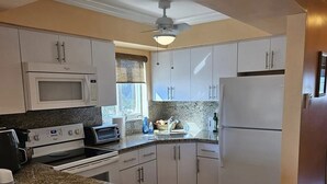 A kitchen with granite countertops, white cabinets, a microwave, stove, and a refrigerator. - Beautiful and Private Oceanfront Condo (Hollywood)