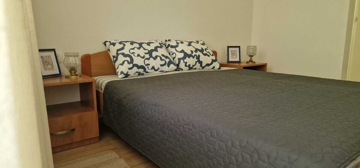 Une chambre à coucher avec un lit, une table de chevet, une lampe et un tableau encadré.