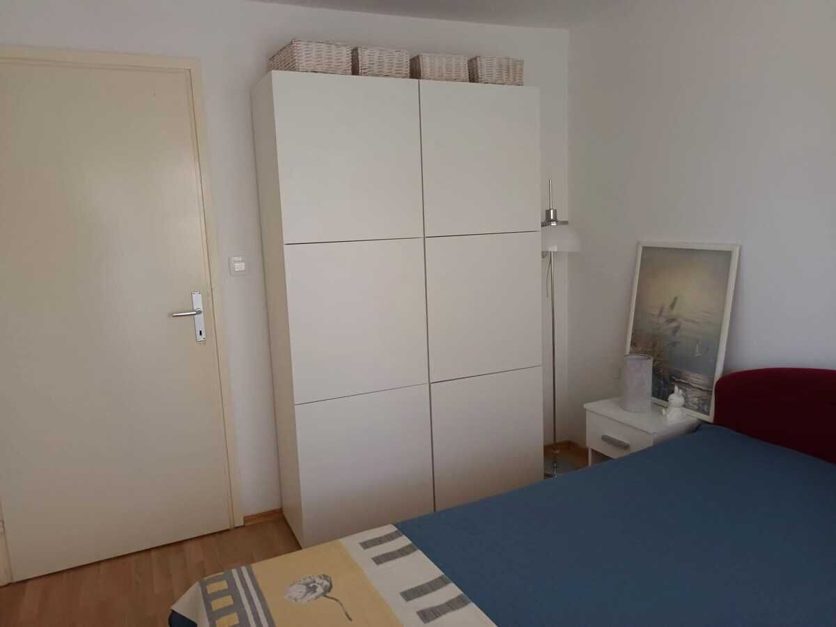 A bedroom with a bed, a wardrobe, a bedside table with a lamp, and a framed picture on the wall.