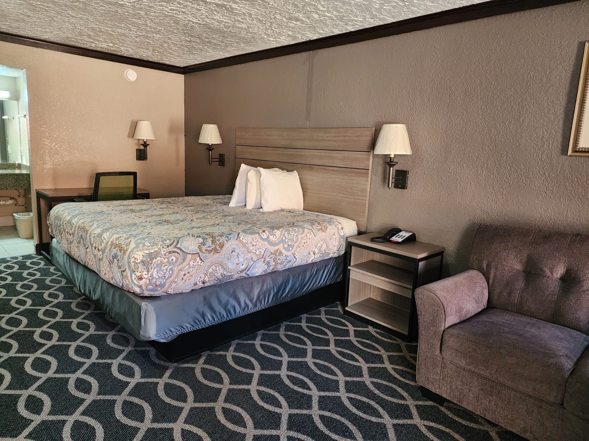 Una habitación de hotel con una cama grande, mesitas de noche, una silla y un escritorio con lámpara.