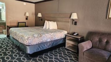 Una habitación de hotel con una cama grande, mesitas de noche, una silla y un escritorio con lámpara.