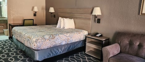 A hotel room with a large bed, bedside tables, a chair, and a desk with a lamp.
