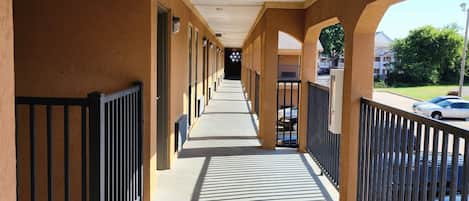 A corridor with an exit sign, metal railings, and a view of parked cars outside.