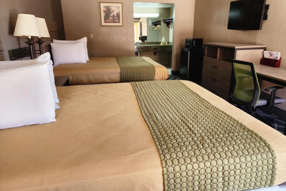 A hotel room with two beds, a desk, a chair, a television, and a mirror.