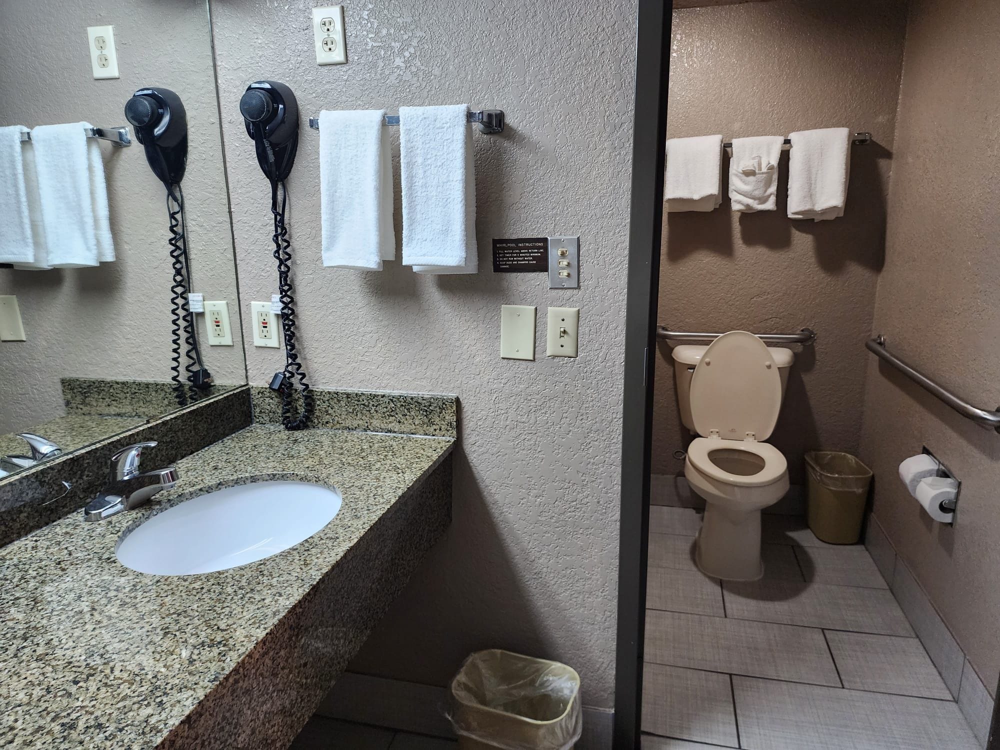 A bathroom with a granite countertop sink, a mirror, a hairdryer, and a toilet.