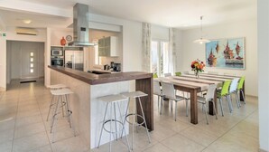 A modern kitchen with a central island, bar stools, and a dining area with a long table and chairs. - Gumonca in Supetar With 6 Bedrooms and 5 Bathrooms (Supetar)